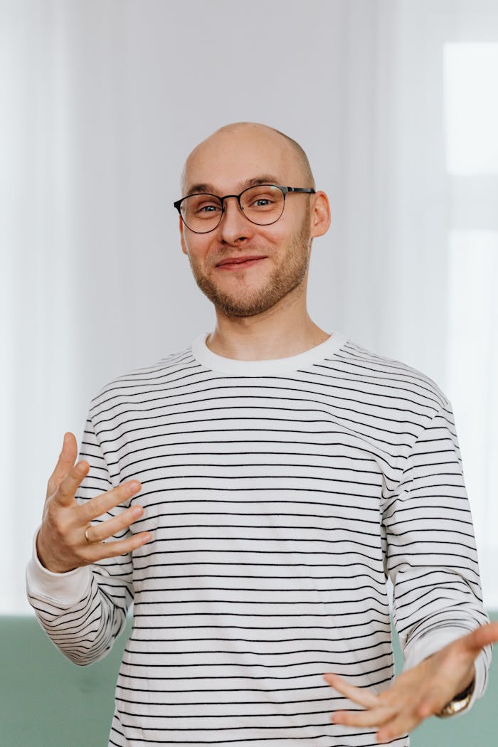 Casual portrait of a smiling bald man with a beard and glasses in a striped shirt indoors.